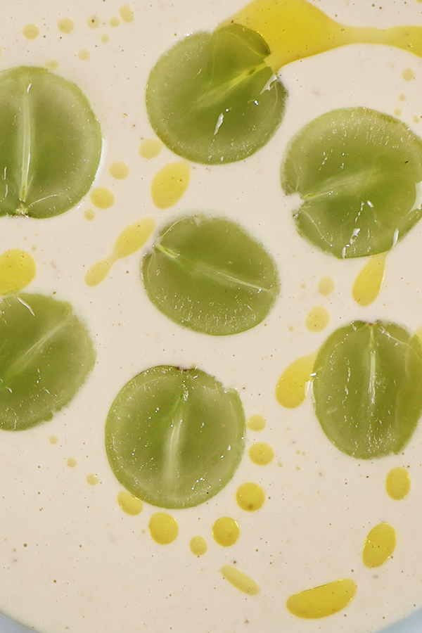 Zbliżenie na kremową zupę z połówkami winogron polaną oliwą z oliwek.