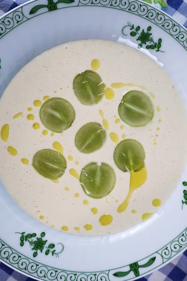 Zbliżenie na talerz i kremową zupę z połówkami winogron polaną oliwą z oliwek.