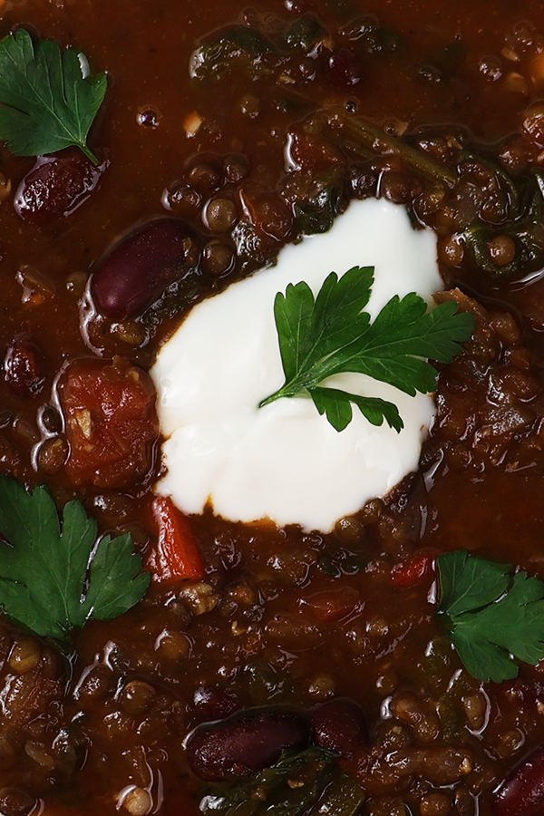 Zbliżenie na zupę z czarną soczewicą, fasolą, śmietaną i pietruszką.