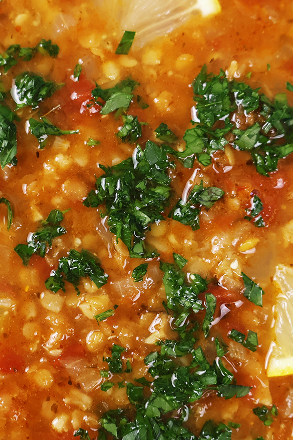 Mocno czerwona zupa, z widoczną kaszą bulgur, kawałkami cytryny i posiekaną natką pietruszki.