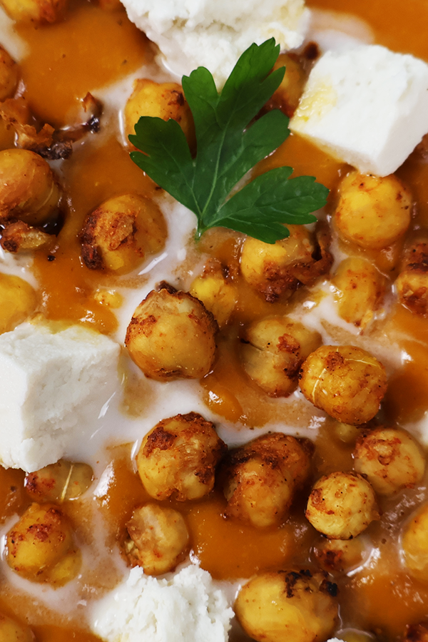 Zbliżenie czerwoną zupę z dodatkiem ciecierzycy, śmietany i pietruszki.