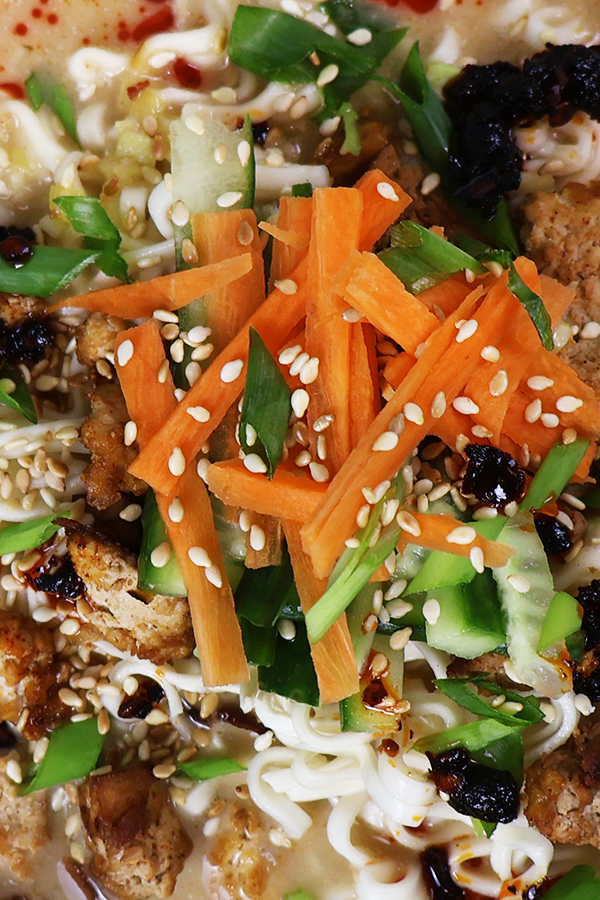 Zbliżenie na zupę z dodatkiem ogórka, marchewki, tofu, szczypiorku, papryki, sezamu i oleju chili.