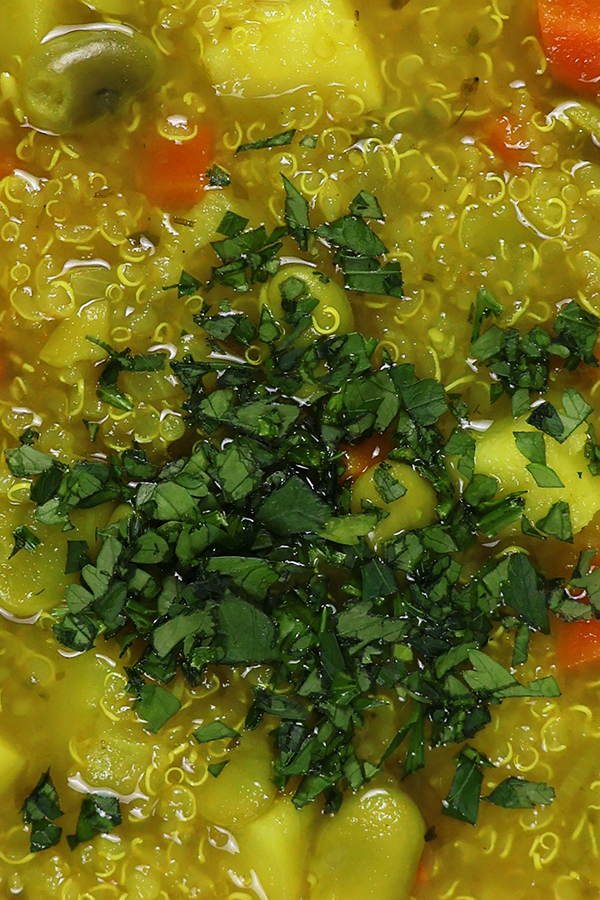 Zbliżenie na kolorową zupę z dodatkiem komosy ryżowej, bobu, ziemniaków i posiekanej pietruszki.