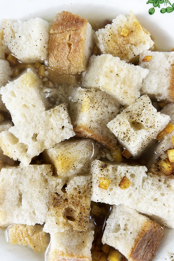 Zbliżenie na kawałki chleba zanurzone w zupie z dodatkiem skwarek z tofu.